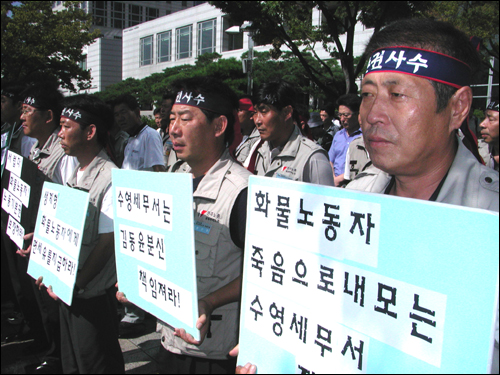 화물노동자들이 12일 오전 부산시청 앞에서 열린 '분신대책위' 기자회견장에 나와 피켓을 들고 서 있다. 